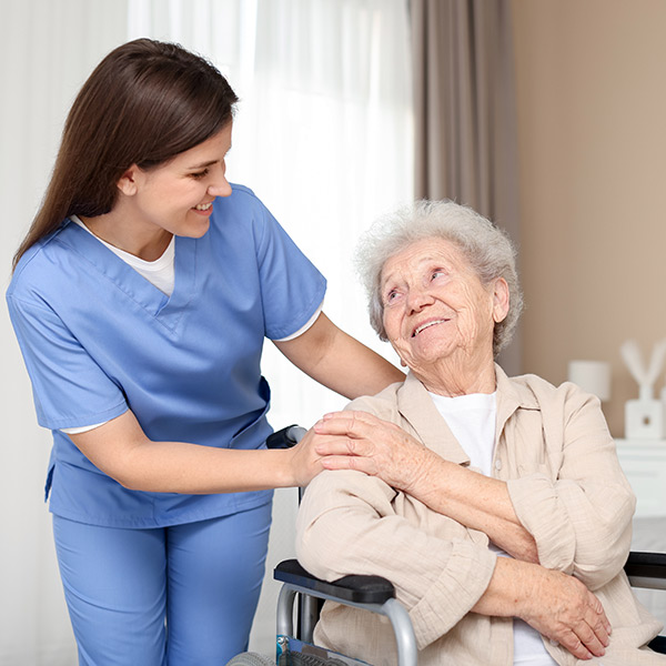 cuidadora con pijama sanitario azul pone las manos en los hombros de una señora mayor