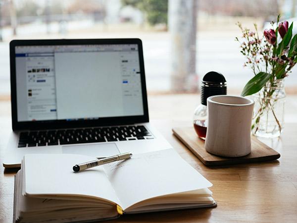 Portátil Macbook mostrando un programa edición de texto junto a un jarrón con flores y una taza