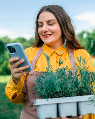 Chica joven con móvil y camisa amarilla recoge macetas con plantas
