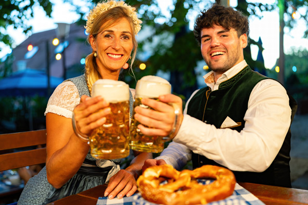 chico y chica con traje tradicional alemán brindando con grandes jarras de cerveza y pretzels