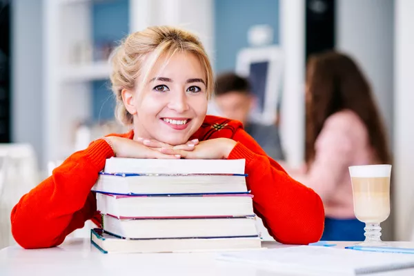 chica rubia con chaqueta roja de punto apoyada en una pila de libros