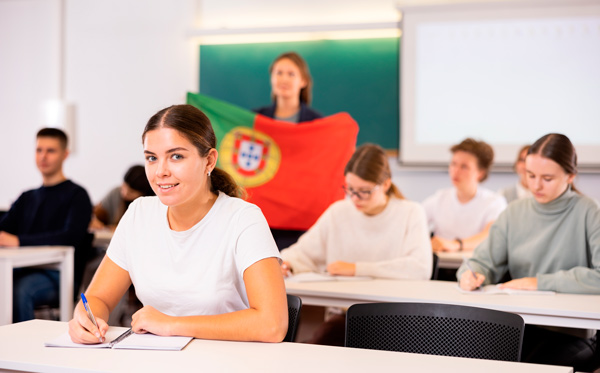 Aula con alumnos estudiando portugués, se ve una profesora con una bandera de Portugal al fondo