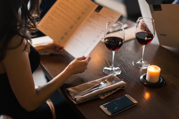 mujer en restaurante tomando vino tinto y revisando la carta de vinos