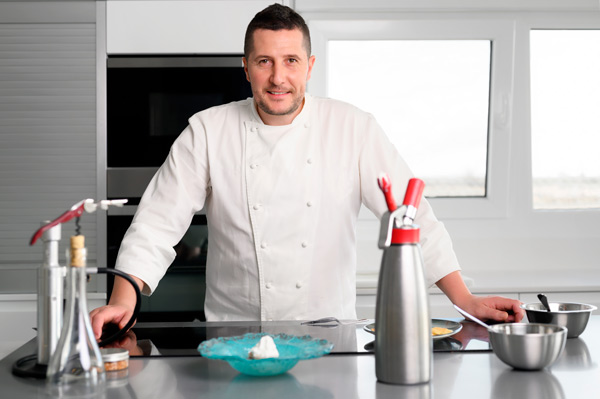 Cocinero posa con equipamiento de cocina creativa, como sifón para espumas y ahumador