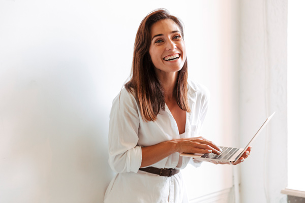 Cursos online gratuitos de Lanbide Mujer joven vestida de blanco con una pared blanca detrás hace un curso online de Lanbide en un portátil