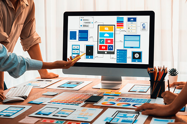 desarrolladores de aplicaciones móviles trabajan en un mac con bocetos de diseño de interfaz