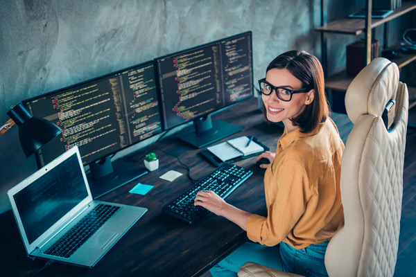 chica joven con gafas delante de varias pantallas de ordenador en las que se aprecia código html
