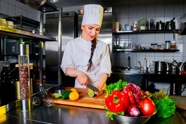 cocinera con trenza prepara verduras en una cocina con azulejos blancos y estanterías de inox