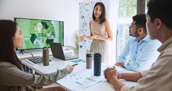 Emprendedora social mostrando su proyecto medioambiental a un grupo de personas en un monitor grande delante de una mesa