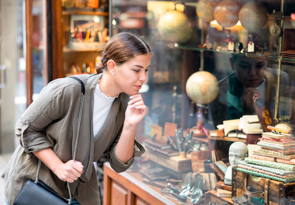 Chica joven con el pelo recogido mira con atención el escaparate de madera de una papelería con libros y bolígrafos