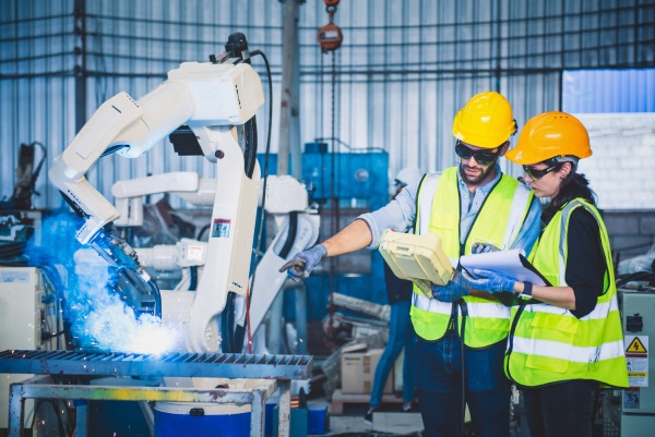 pareja de trabajadores controlando un robot industrial en una factoría