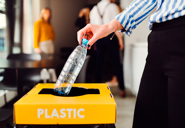 Mano de mujer envía una botella de agua de plástico al contenedor amarillo de reciclaje