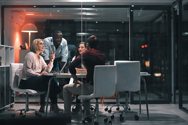 Reunión de directiva con su equipo en un despacho acristalado de una empresa, con la luz baja