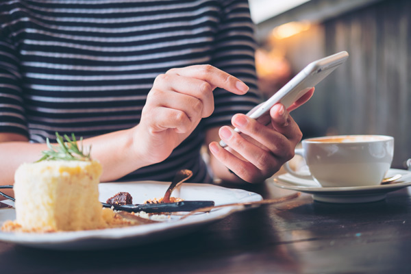 persona realizando pedido de comida en su móvil, mientras toma un plato de cocina innovadora