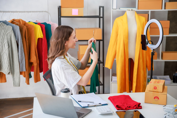 Chica joven enseñando a la cámara de un móvil ropa de su tienda para generar contenido