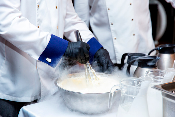 cocineros trabajando una crema en un bol con nitrógeno líquido