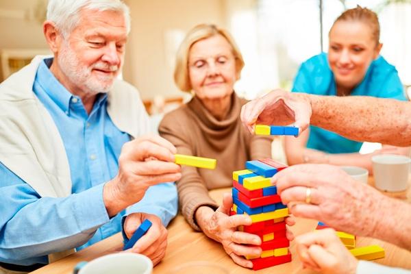 Mayores jugando a un juego de mesa en una residencia, junto a su cuidadora