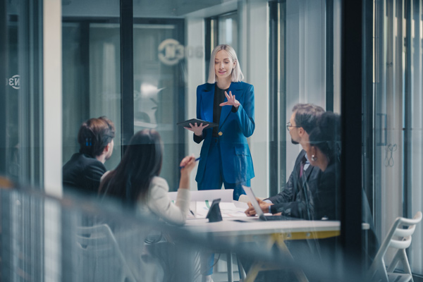 Líder tecnológica da una charla a su equipo en una sala de reuniones acristalada con una tablet en la mano