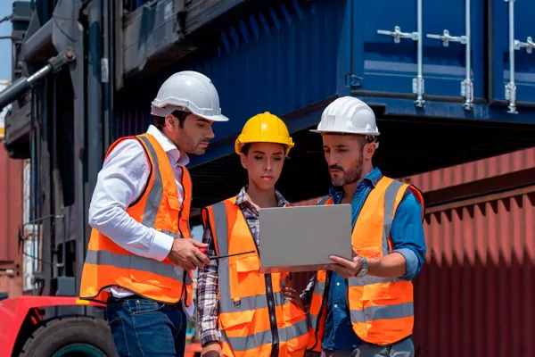 operarios de logística con un portátil delante de un grupo de contenedores para transporte internacional