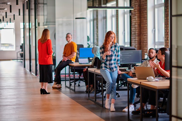 Espacio de coworking con amplios pasillos y paredes de ladrillo donde trabajan jóvenes en régimen de coworking, se ven mesas, ordenadores y jóvenes hablando.