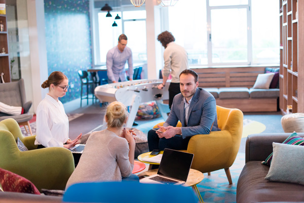 reunión de dos chicas jóvenes con un inversor en un espacio coworking con sofás de colores