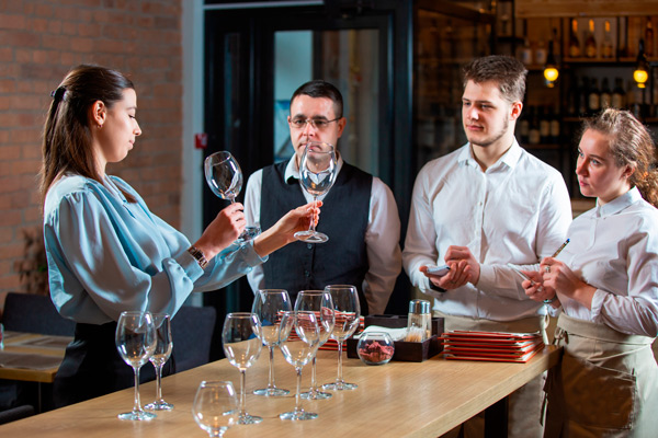 mujer sumiller alecciona a su equipo sobre diferentes copas para el servicio del vino en un restaurante