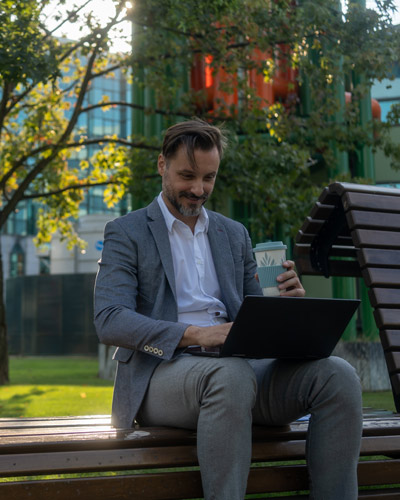 Cursos online gratuitos hombre con traje realizando un curso online en un banco del parque con un portátil