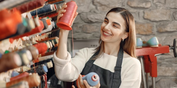 Chica sastre eligiendo dos carretes de hilo para fabricar prendas de vestir