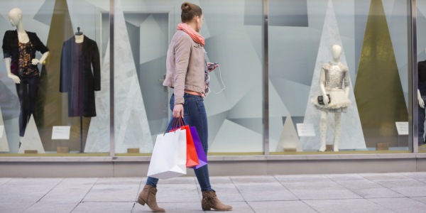 Chica joven pasa frente a escaparate de una tienda y se detiene a ver la colección